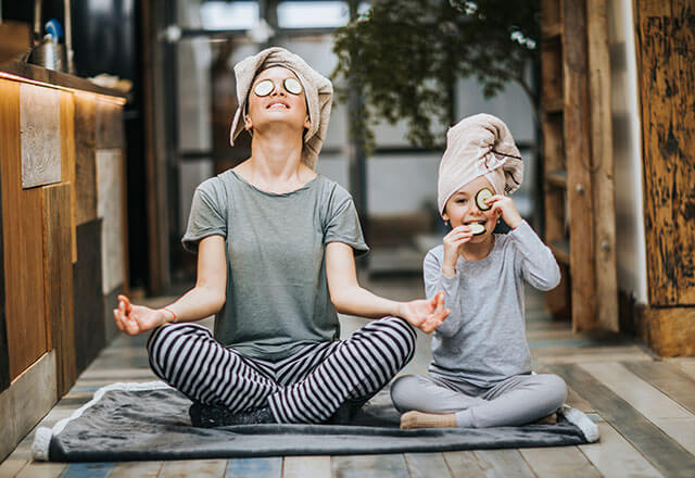 a mother and daughter do yoga and meditation together as the daughter eats a cucumber slice
