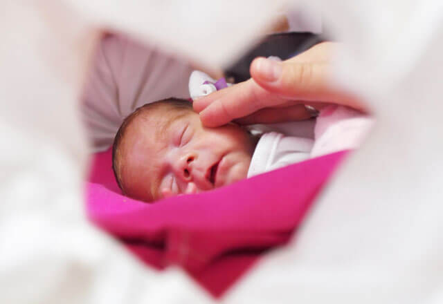 a hand touches the face of a tiny infant