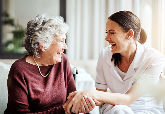 doctor sitting down holding hands with smiling older patient
