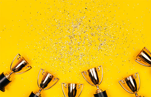bunch of trophies with confetti on a yellow background