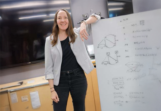 Alexis Battle, Ph.D. standing next to a white board with written formulas.