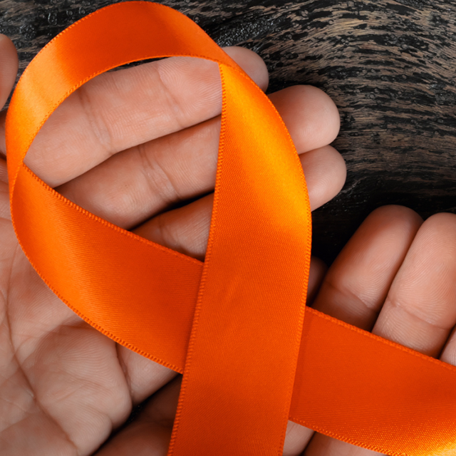 Hands holding an orange ribbon representing skin cancer awareness.