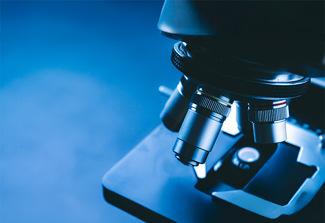 Close-up of a microscope lens in a lab, highlighted in blue tones. The focus is on the metallic lenses, conveying precision and scientific inquiry.