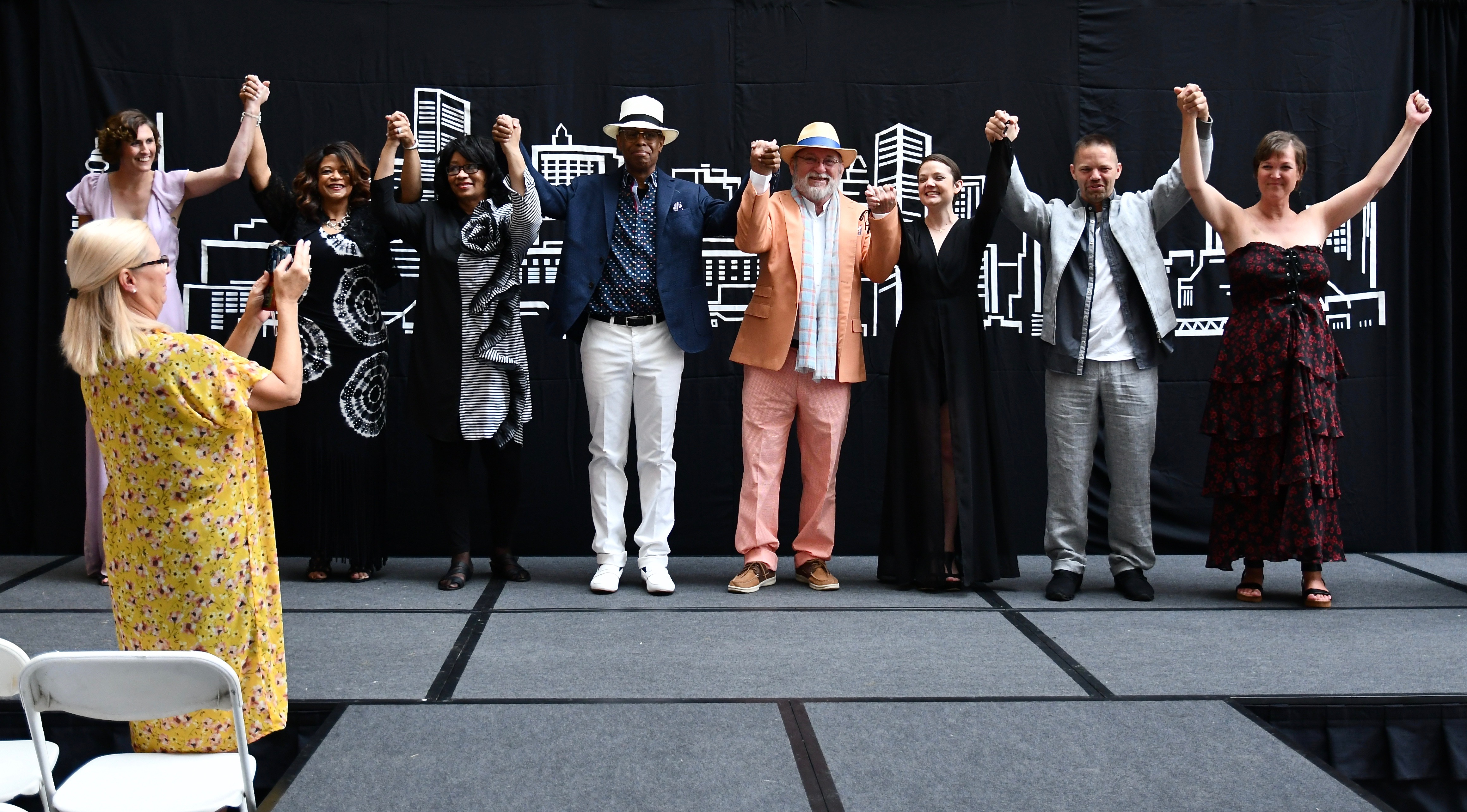 Group of fashion show models/survivors holding each other's hands up.