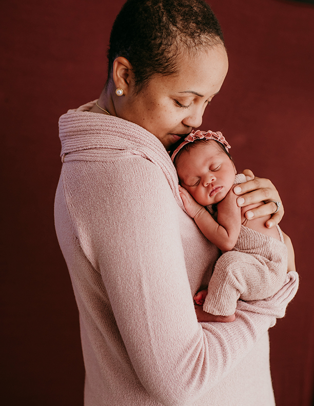 Amanda in a pink sweater holding her baby girl in matching sweater.