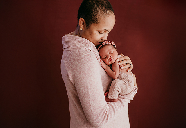 Amanda in a pink sweater holding her baby girl in matching sweater.