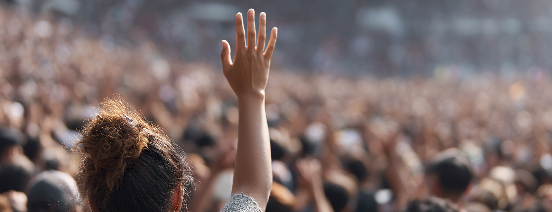 Enthusiastic crowd with raised hand at a live event, conveying excitement and participation at a public gathering. 