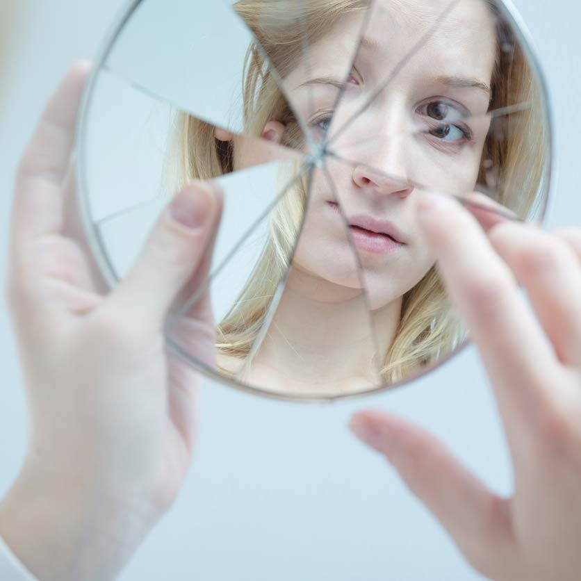 Girl looking at her reflection in a broken mirror