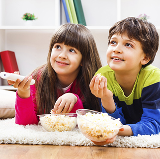 Two children eating popcorn while watching TV