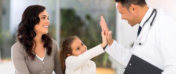 A mother smiling as her daughter gives a doctor a high five