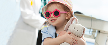 A girl wearing sunglasses shaped like flowers smiles and waits with her doctor nearby at Johns Hopkins All Children's Hospital.