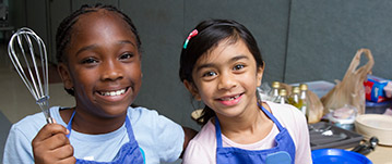 Two little girls smiling in a cooking class.