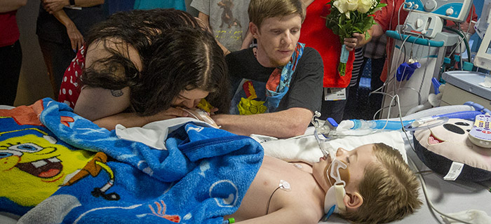 An unconscious boy in a hospital bed breathing through a respiratory with his mother and brother watching over him at Johns Hopkins All Children's Hospital in Florida
