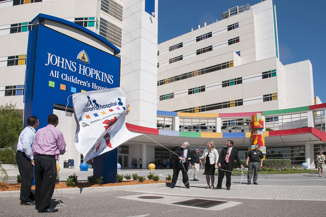 Members of the hospital leadership team outside the hospital pulling back a banner to reveal the hospital's new name Johns Hopkins All Children's Hospital and new logo