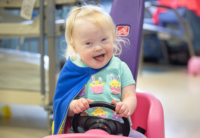 Shelby riding in her toy car in her room at Johns Hopkins All Children's