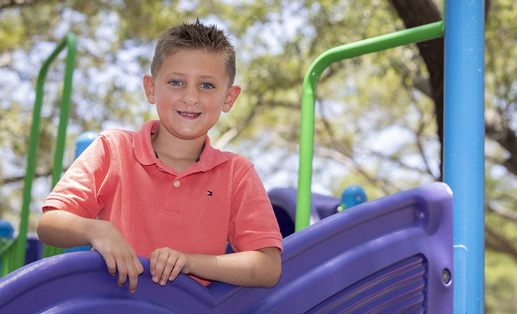 Patient Logan playing outside at a park on playground equipment