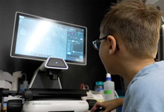 A boy sitting in a science lab and looking at a computer screen