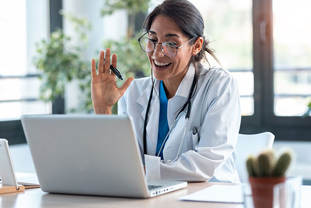 A woman doctor waving at a patient through the laptop
