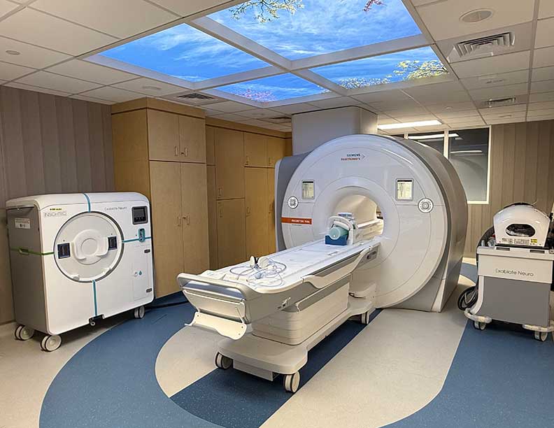Modern MRI room with scanner, blue and white color scheme, and a calming ceiling mural of clouds and trees. The setting is clean and clinical.