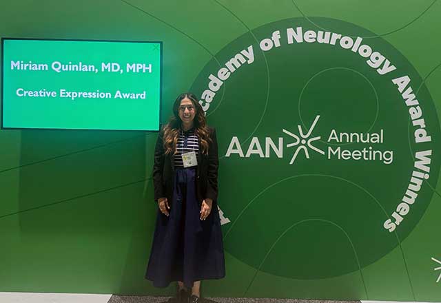 A woman stands in front of a green backdrop displaying text about the Academy of Neurology and Miriam Quinlan, MD, MPH recognized with the Creative Expression Award.