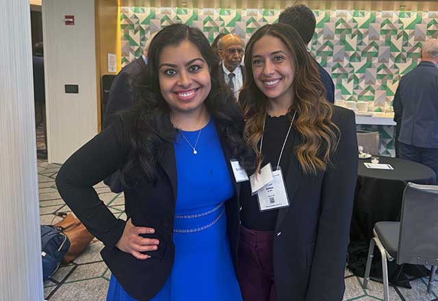 Two women dressed in business attire stand side by side, posing for a photo with smiles, exuding professionalism.