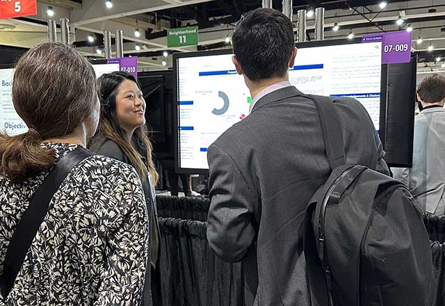 Three people at a conference engage with a digital presentation on a screen. The atmosphere is focused and collaborative, with vibrant lighting.