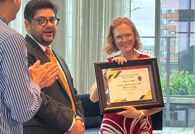 Dr. Muehlschlegel smiles and holds the framed Faculty Mentor of the Year Award