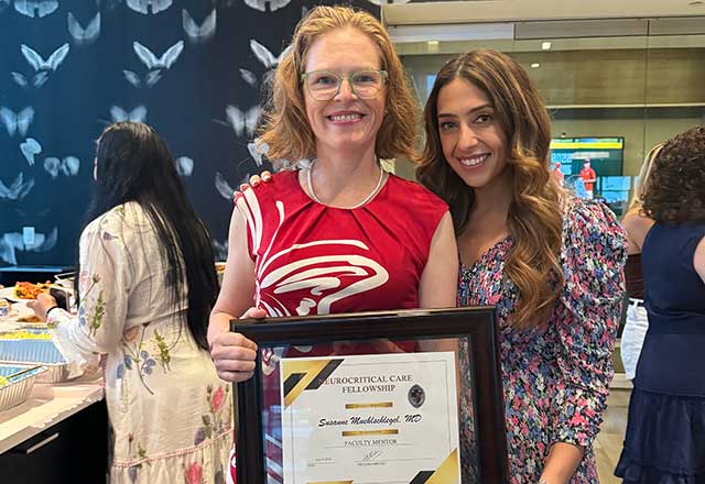 Dr. Muehlschlegel and a graduating lab member smile and hold the framed Faculty Mentor of the Year Award