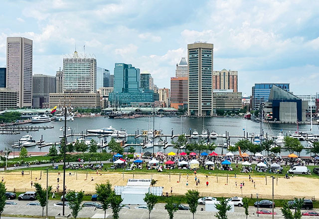 Picture of the Baltimore Inner Harbor during the day, with the volley ball courts in view.