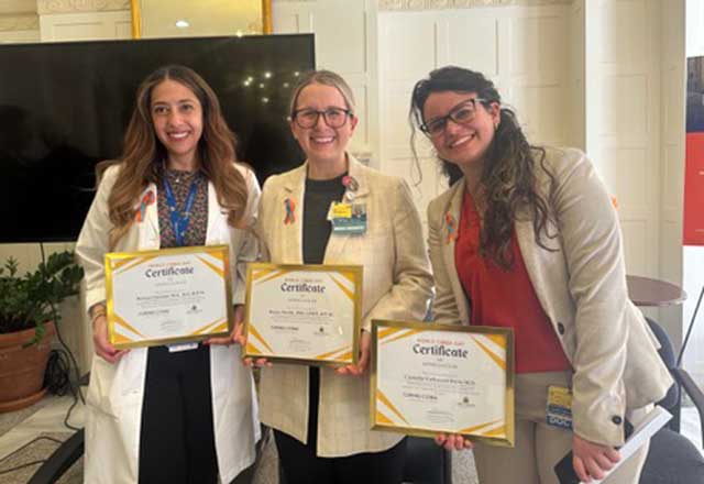 Three women in lab coats proudly display their certificates, celebrating their achievements in a conference setting.