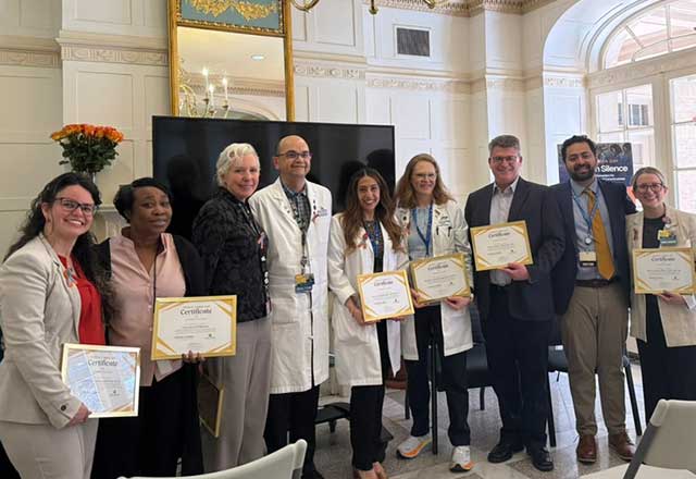 A group of healthcare professionals, some in white coats and a few in suits, proudly displaying their certificates in a celebratory setting.
