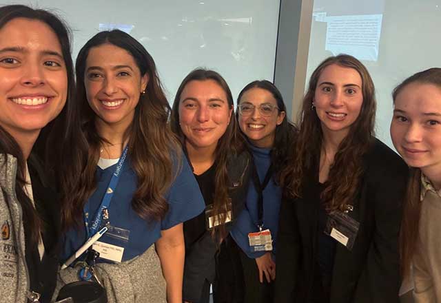 Several women of different backgrounds standing in a medical office, smiling and posing for the camera.