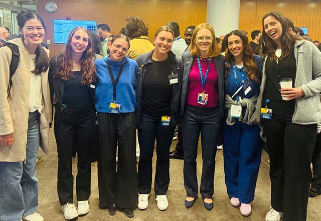  A group of women standing together in a conference room, smiling for the camera, with presentation screens behind them.
