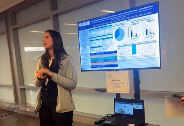 A woman stands confidently presenting in front of a large screen displaying graphs and data.