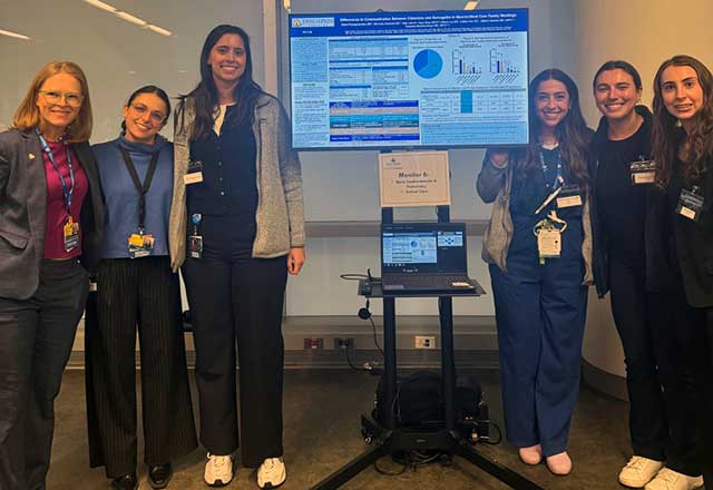 Six women stands together, three on each side of a large screen, which shows graphs, charts and other data.