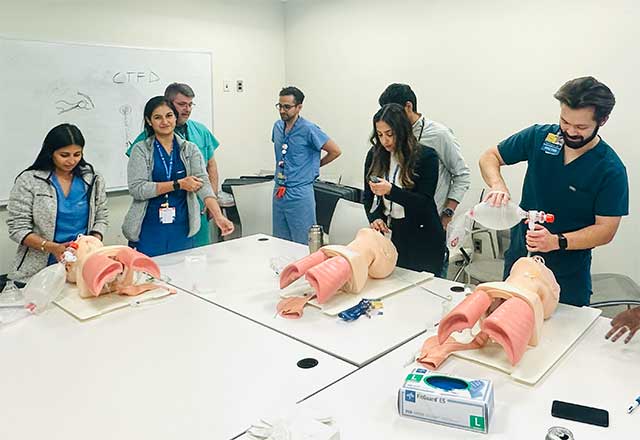 NCC fellows practice CPR on torso mannequins in a bright classroom. With focused expressions, they engage in hands-on training, supervised by a facilitator.