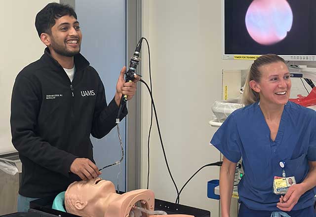 Two medical professionals, one holding an endoscope, practice on a dummy head. Both are smiling, suggesting a collaborative, positive environment.