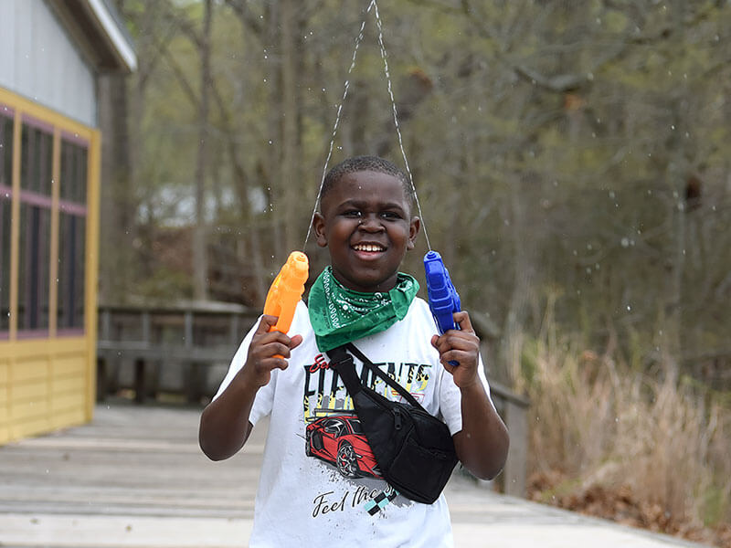 young boy squirting water guns at camp