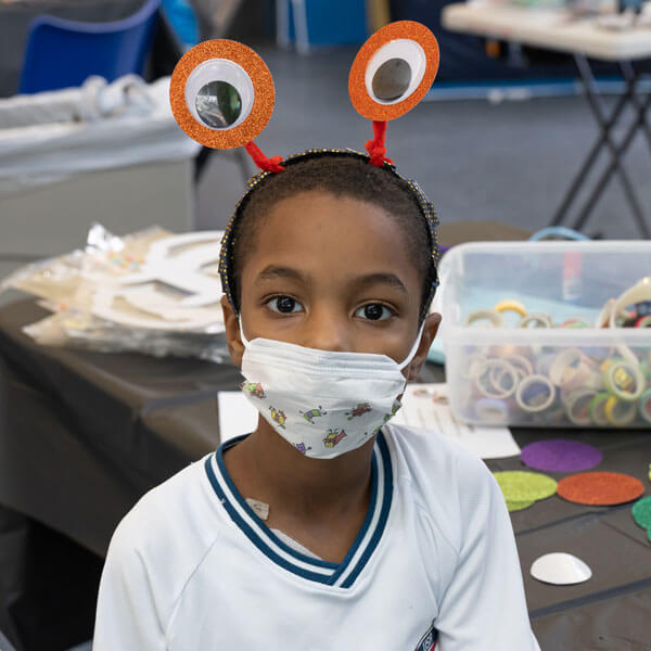 young child with a mask and fun headgear with eyeballs