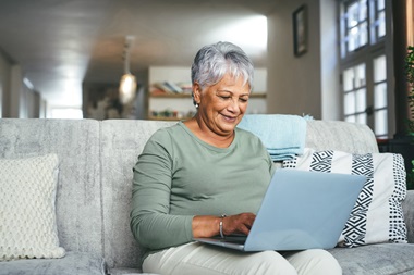 A woman sits on a couch in a living room while using her laptop