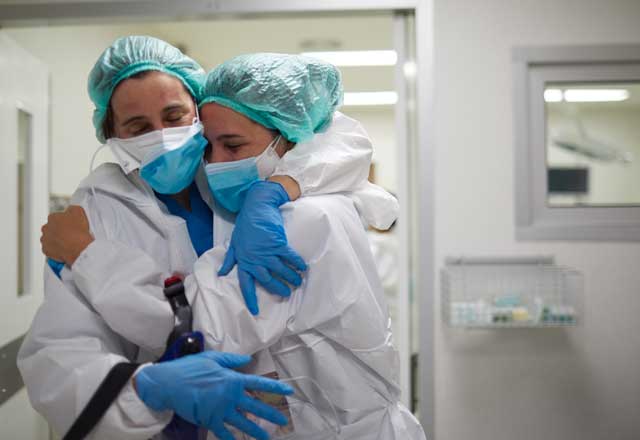 Two health workers in PPE hugging each other
