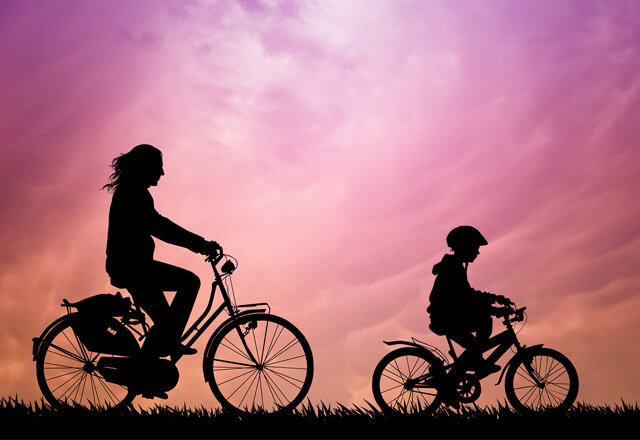 Eva and her son in silhouette, riding their bikes in the sunset.