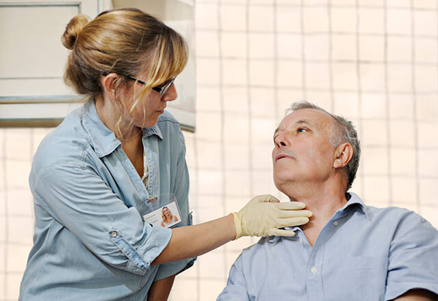 A speech therapist checks a man's throat.