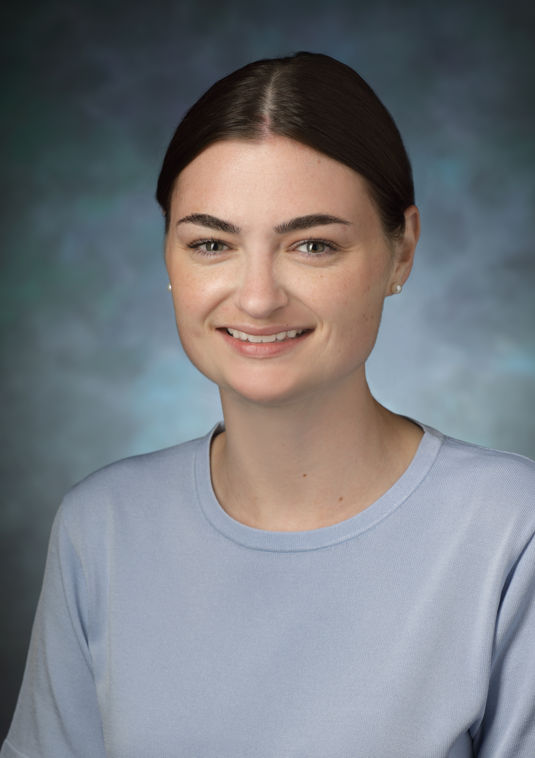 Samantha Ernst, wearing a pale blue top, smiles in front of a blue photo backdrop