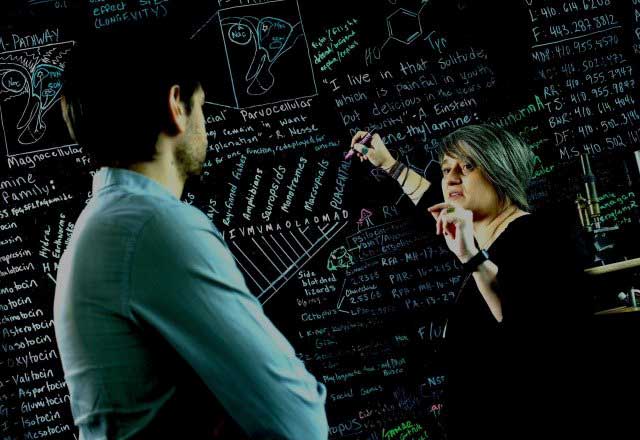 Researcher writing on a blackboard with chalk and talking to a colleague. 