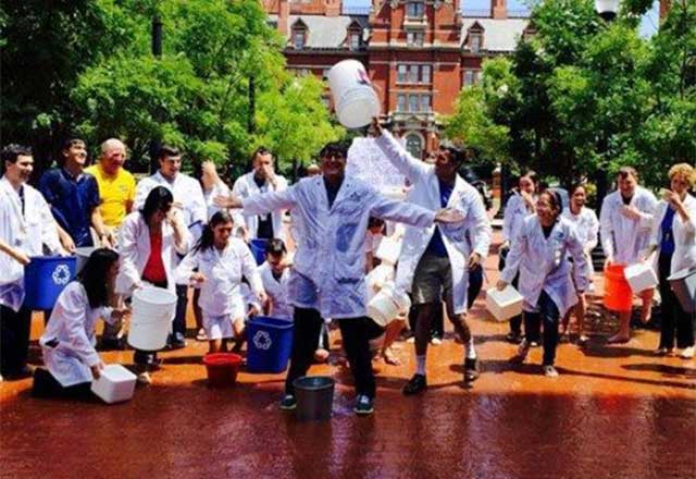 Healthcare providers standing outside with a large water bucketing being poured over one of their heads.