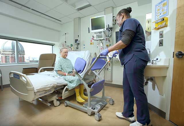 A healthcare worker helping a patient out of bed using a mobility device.
