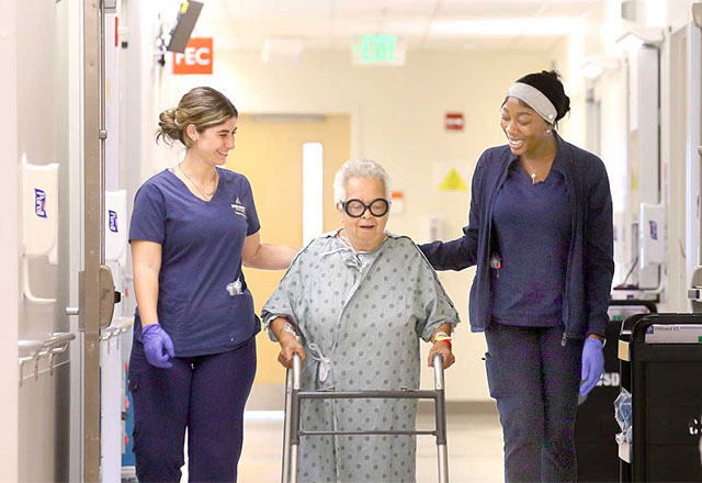Two health professionals assisting a patient with a walker.