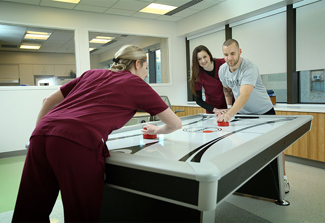 A patient playing air hockey with a therapist with another therapist helping the patient.