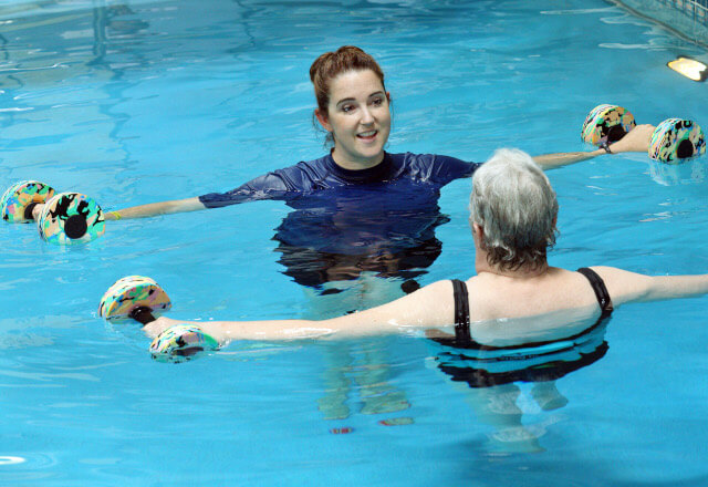 a woman works with a therapist in a pool during aquatic therapy
